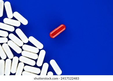 Large number of white pills scattered on a blue surface, among the white pills a single red pill drawing focus, symbolically representing uniqueness or distinction