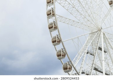 A large observation wheel with multiple passenger pods is captured against a backdrop of overcast, gray clouds, creating a dramatic scene