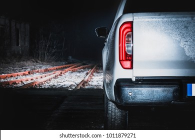 A large off-road white pickup truck. A view of the off-road car at night on the railway tracks. View of the back of the car, in front of the car, a railway crossing.