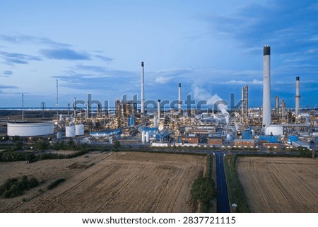 Large oil refinery facility processing energy resources with tall smokestacks and storage tanks during the evening light under a blue sky