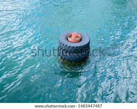 Large old black tires being used as bumpers at concrete dock, partially submerged in blue water.
