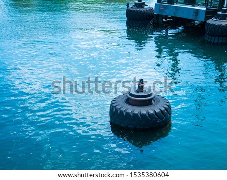 Large old black tires being used as bumpers at concrete dock, partially submerged in blue water
