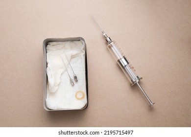 A Large Old-style Glass Syringe And A Metal Box Of Syringes On An Old, Dirty Table.