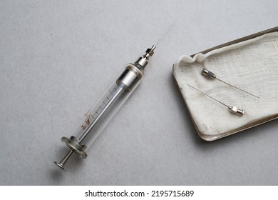 A Large Old-style Glass Syringe And A Metal Box Of Syringes On An Old, Dirty Table.