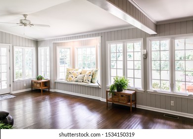 Large and open living room den sun room with windows on two sides and lots of natural light flowing in. There is a window seat on one side and a leather couch and plant on the other. - Shutterstock ID 1534150319