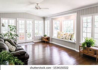 Large and open living room den sun room with windows on two sides and lots of natural light flowing in. There is a window seat on one side and a leather couch and plant on the other. - Shutterstock ID 1534150322