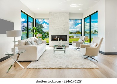 large open living room with lake view floor to ceiling windows view granite fireplace white furnishings hardwood floor and white area rug - Shutterstock ID 2246176129