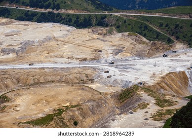 Large open-pit mining site with heavy machinery. Earth-moving vehicles operate across rocky terrain. Dirt roads connect different excavation zones