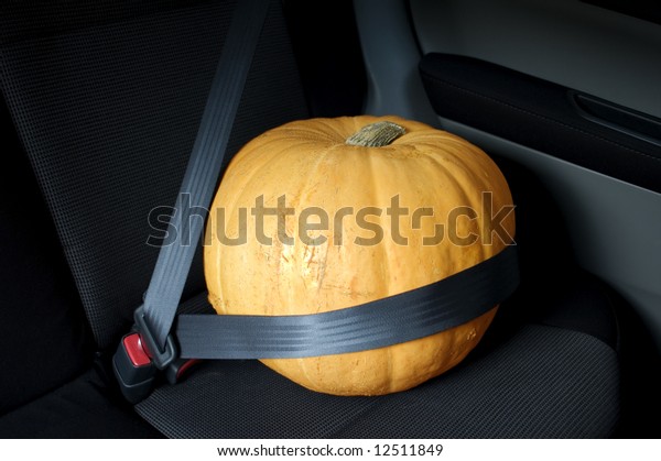 Large orange Halloween pumpkin sitting in car\
with seat belt. Could also be used as conceptual photograph for\
food transport.
