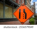 Large orange lane closed merge sign on urban sidewalk space for copy.