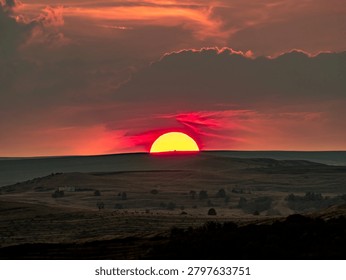 Large orange sun setting behind distant hills under dramatic sky