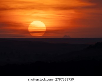 Large orange sun setting behind distant hills under dramatic sky