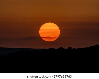 Large orange sun setting behind distant hills under dramatic sky