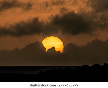 Large orange sun setting behind distant hills under dramatic sky