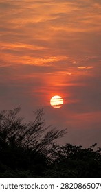 large orange sun setting behind clouds over trees silhouette at sunset