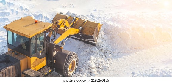 A large orange tractor removes snow from the road and clears the sidewalk. Cleaning and clearing roads in the city from snow in winter. Snow removal after snowfalls and blizzards. - Shutterstock ID 2198260155