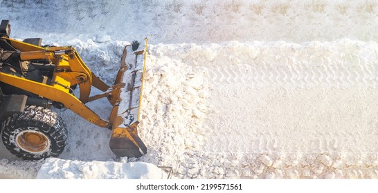 A large orange tractor removes snow from the road and clears the sidewalk. Cleaning and clearing roads in the city from snow in winter. Snow removal after snowfalls and blizzards.