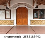 A large, ornate wooden door stands out against the white facade of a traditional Indonesian house.