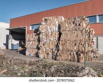 Large packages of paper and cardboard stacked and compressed at great heights outside a building for later recycling at a paper recycling plant