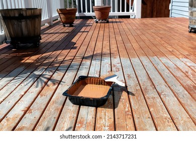 Large Paint Brush Resting On Top Of Tray With Stained Cedar Wood Deck Boards In Background