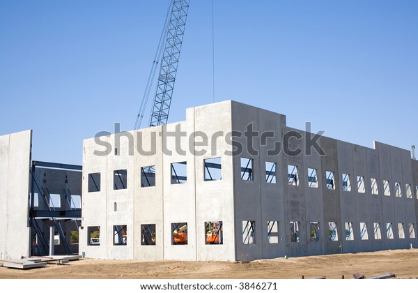 Large panels of precast\
concrete are tilted up with cranes to form the walls of a large\
building