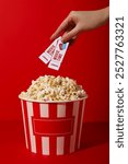 Large paper cup of popcorn and movie tickets in hand on red background