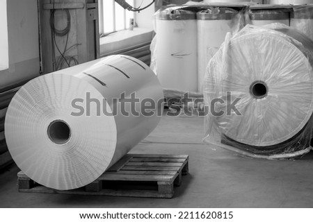 Large paper roll for typography. Flexographic white self-adhesive paper for the production of labels with color printing. Warehouse of materials in printing house. Jumbo roll. Selective focus