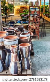 Large patterned ceramic urns and flower pots arranged on wooden pallets inside a nursery greenhouse with shelving units in the background.