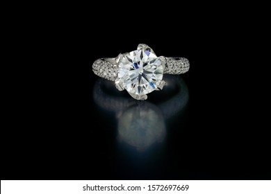 A large perfect cut diamond is held by five prongs of platium in this solitar ring. The ring's shoulder are pave' with diamonds. Shown on a black reflective background.