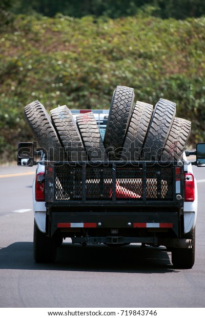 A large pickup truck transport used tires with large\
tread pattern for big rig semi trucks in its dump moving along a\
picturesque road