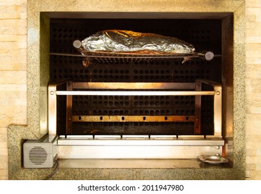 Large Piece Of Rib Wrapped In Tin Foil, Slowly Roasting On The Wood Fire Of The Barbecue Grill. Brazilian Barbecue.