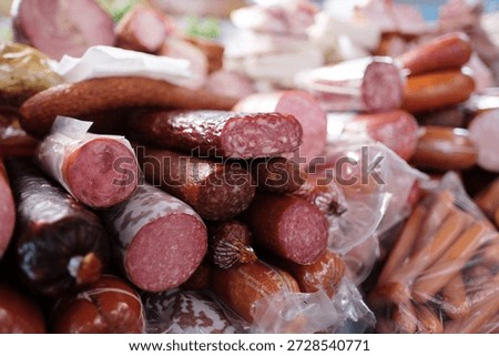 A large pile of assorted cured meats and sausages, including salami, smoked sausages, and frankfurters, stacked on display at a market butcher stall.