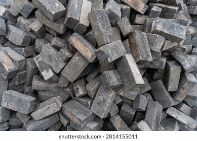 Large pile of dark gray rectangular concrete paving blocks stacked loosely at a construction site. Weathered paving stones with rough textured surfaces create a detailed background suitable for road construction, landscaping, driveway installation, sidewalk paving, and urban infrastructure concepts.