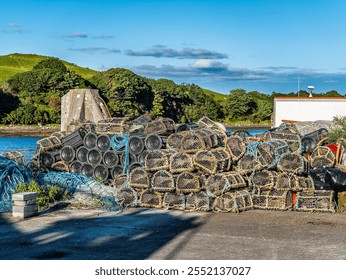 A large pile of fishing nets and traps is stacked by the riverside, with lush greenery and a clear blue sky in the background, depicting a serene and industrious scene. - Powered by Shutterstock