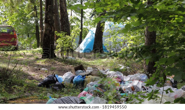 A large pile of garbage next to a \
camp tent and car in the forest woods on a Sunny summer day,\
littering the environment with tourists social\
issue