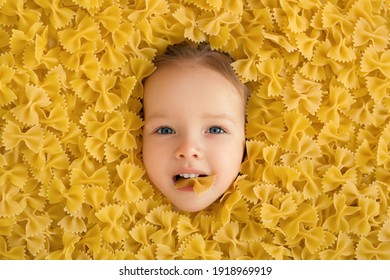 large pile of noodles in the form of a bow. The child eats pasta. Pasta made from durum wheat. The baby's face is surrounded by a large amount of macaroni. Beautiful baby blue eyes.