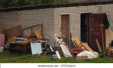 A Large Pile Of Old Unnecessary Things And Furniture Thrown Outdoor Next To A Abandoned Brick Barn In The Village, General Cleaning In The Yard On A Summer Day