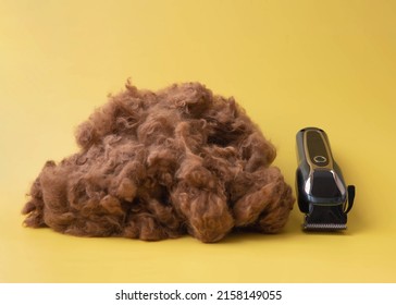 a large pile of shorn brown dog hair next to a dog clipper on a yellow background.