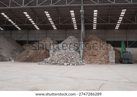 Large piles of sorted construction materials inside recycling warehouse with industrial loader, waste processing and circular economy concept