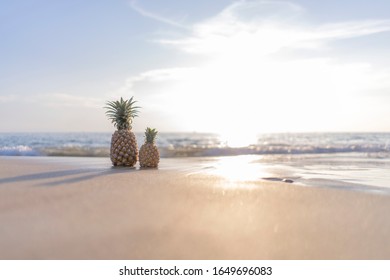 A large pineapple and a small pineapple stand on the sand against the background of the sea and sunset. Photo is ideal for advertising, poster and wallpaper