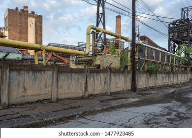 Large Pipes Running Along A Large Concrete Wall In Front Of An Abandoned Blue Collar Industrial Factory In A Small Rust Belt Town In West Virginia