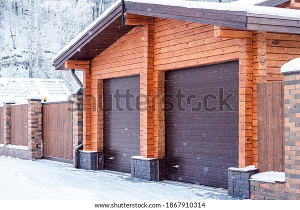 Large plan light brick garage for two cars with\
automatic gates in a winter village, soft focus and snowfall.\
Winter country life