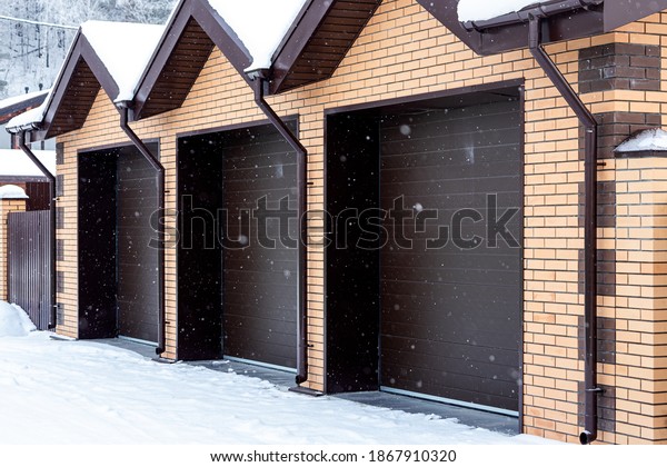 Large plan light brick garage for three cars with\
automatic gates in a winter village, soft focus and snowfall.\
Winter country life