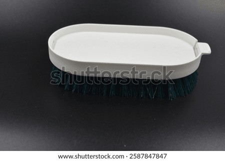 A large plastic oval white brush with green bristles for cleaning carpets, things is located on a black plastic background.