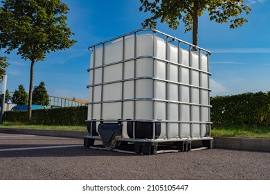 Large plastic tank for liquid. White square barrel for water. Liquid tank in metal lining. Water tank is on street. Light container for water. Huge container with reinforced mesh.
