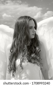 A large portrait of a beautiful girl with long hair in the image of an angel with white wings. Black and white photo, monochrome.