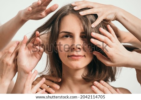 A large portrait of a beautiful girl. Lots of hands around a woman's face. The impact of society on modern man