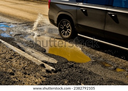 Large pothole in city street creates hazardous driving conditions for passing vehicles.
