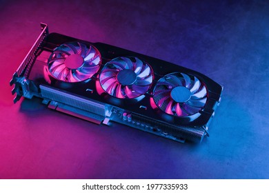 Large and powerful graphics card with three fans with blue pink light. The concept of a cyberpunk video chip for gaming and cryptocurrency mining. Dark key, top view
