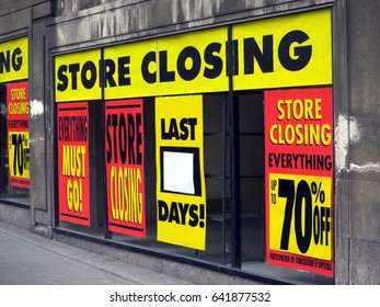 Large printed signs in a department store window announcing store closing and price reductions.